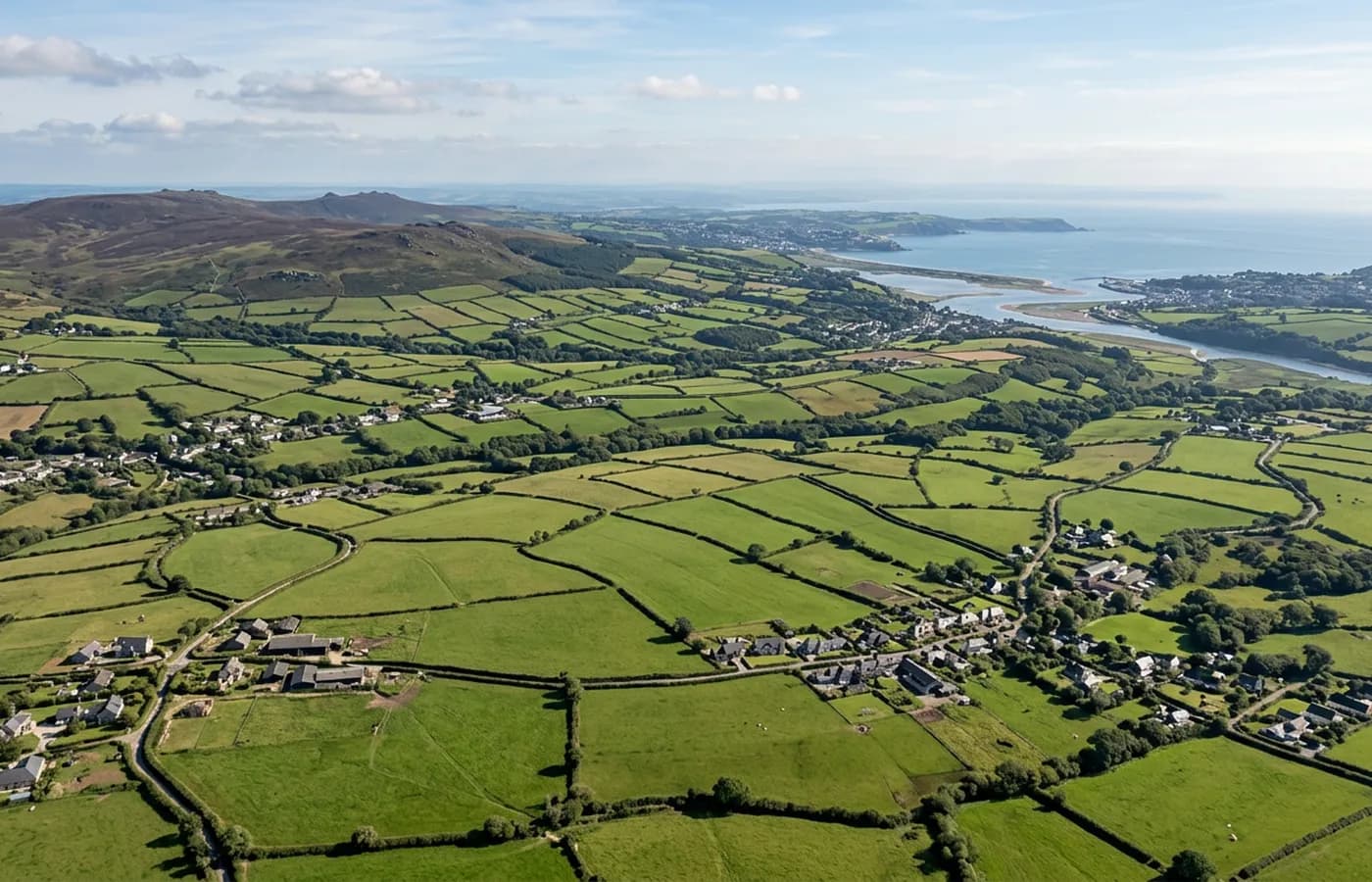 A high aerial view across the South West of England showing hedged fields and small settlements running towards a distant estuary with moorland on the horizon
